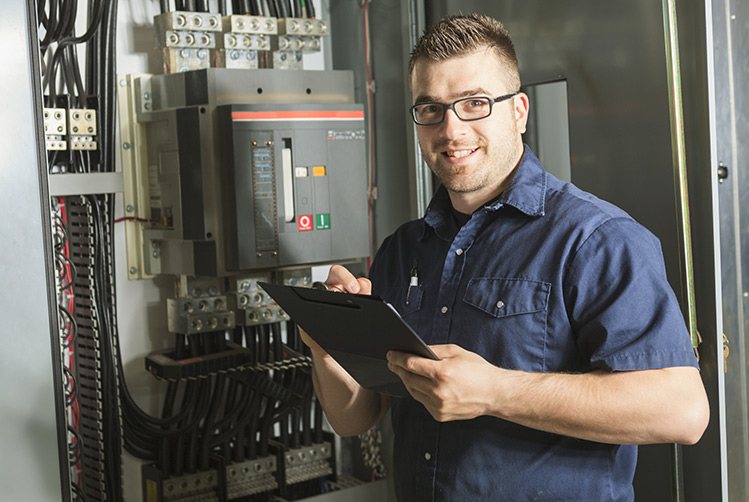 An electrician with a clipboard standing at an electrical panel
